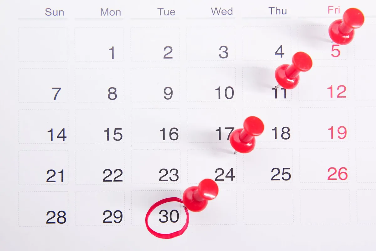 A paper month calendar with red push-pins in several dates and the 30th circled in red