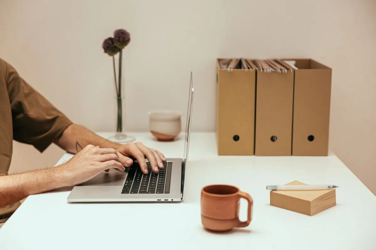 Hands typing on a laptop at a white desk with archive file boxes behind it