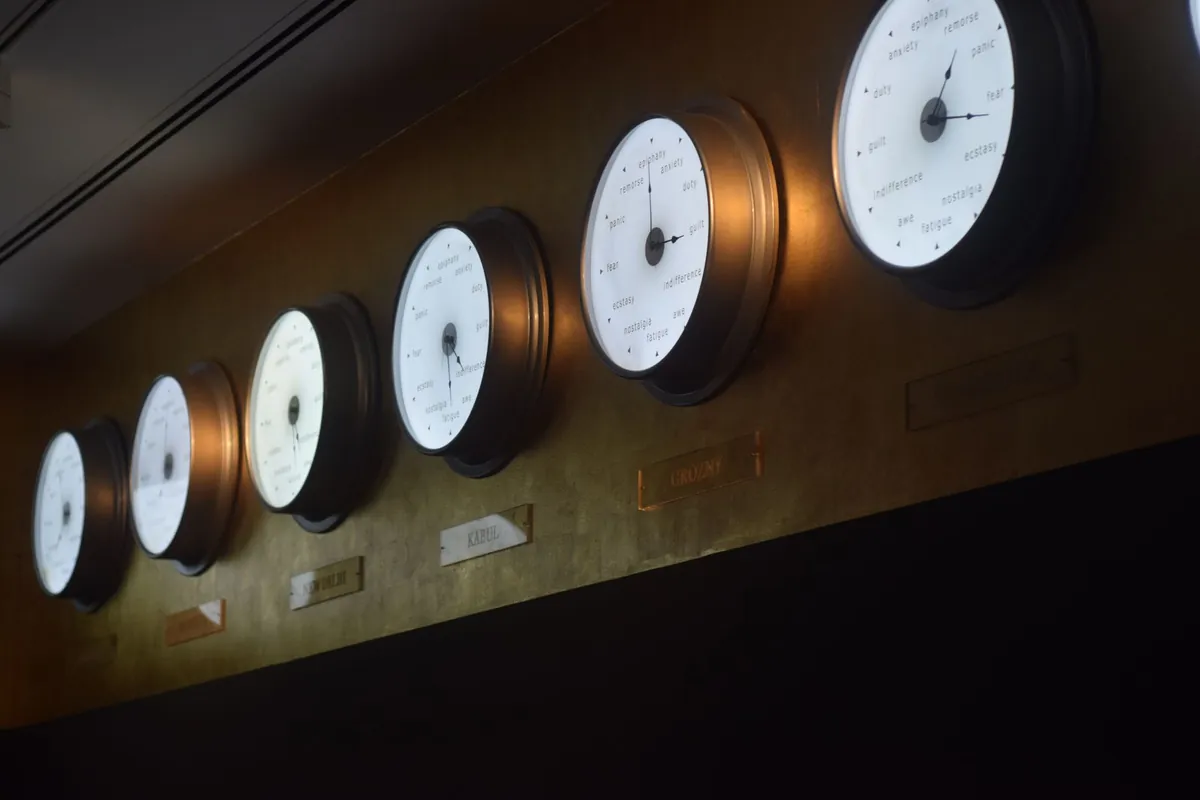 A row of round wall clocks along a dark wall, each showing a different time
