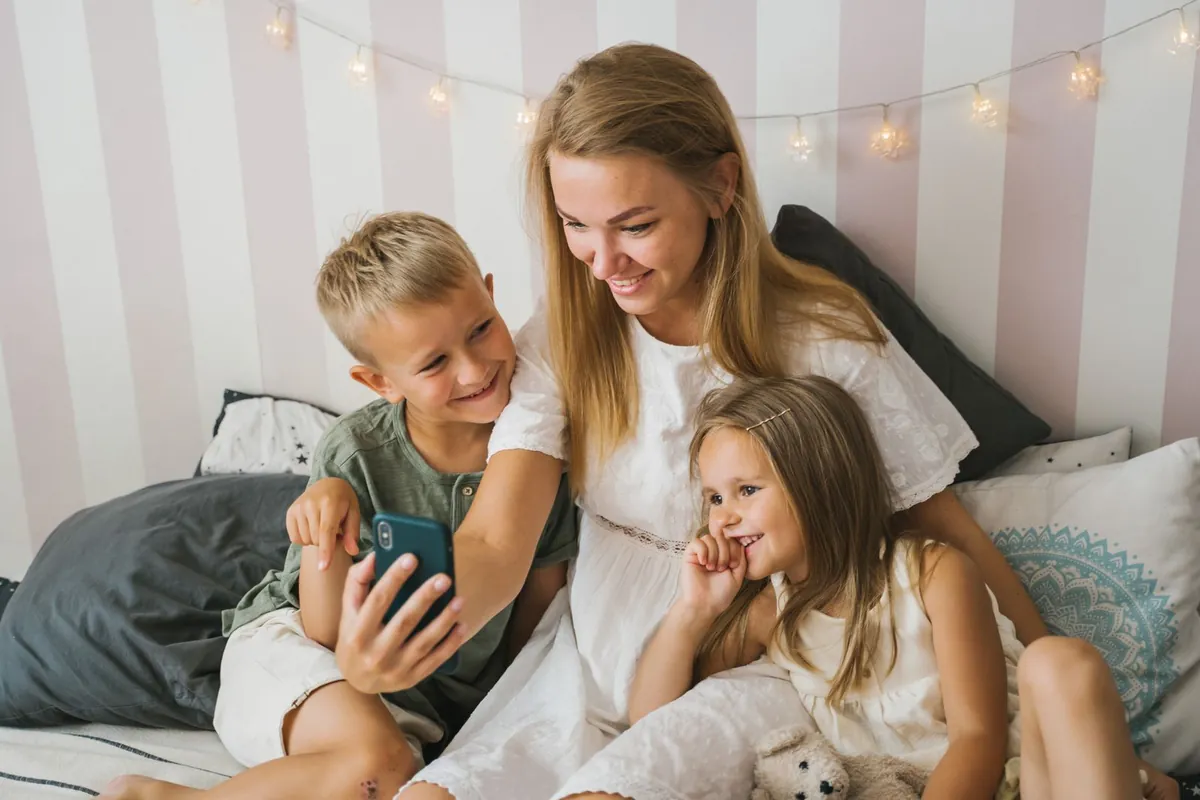A mother and two children sitting on a bed, the boy showing her something on a phone